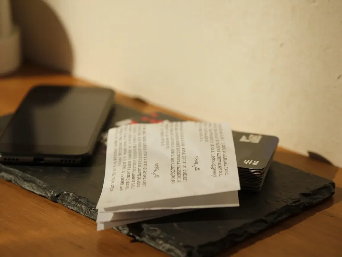 Blurred paper receipt on a slate coaster beside a face-down phone and unused cards